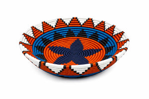 Vibrant handwoven decorative basket bowl with geometric orange, blue, and white patterns on a white background.