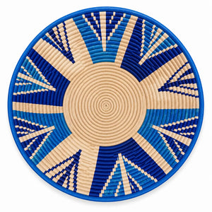 Handwoven round wall basket with blue and beige geometric sunburst pattern. African-inspired home decor.